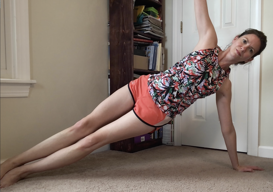 Picture of a female MotivateU fitness instructor completing a side plank looking forward and facing the camera smiling with a white door and bookshelf behind her.